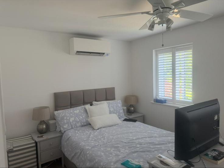 Wall-mounted AC unit installed in a bedroom with shutters