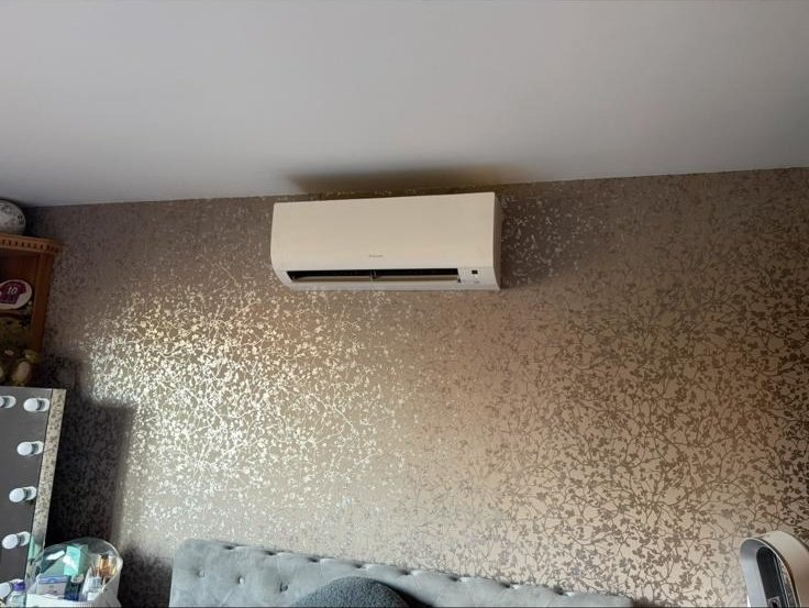 Wall-mounted AC unit installed in a bedroom with a metallic patterned feature wallpaper