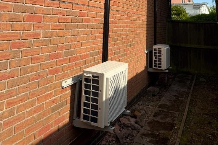 Two outdoor condenser units installed side by side on a brick wall