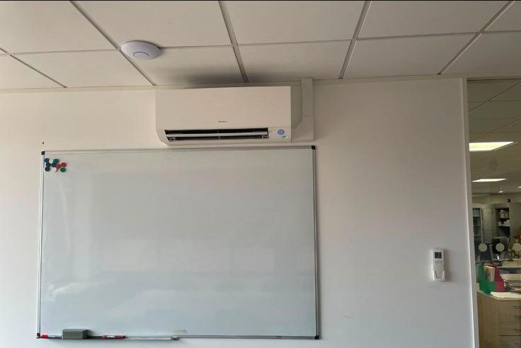 Wall-mounted AC unit installed in an office above a whiteboard